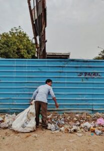 A man collects trash in a vibrant urban setting, highlighting waste management in Noida, India.